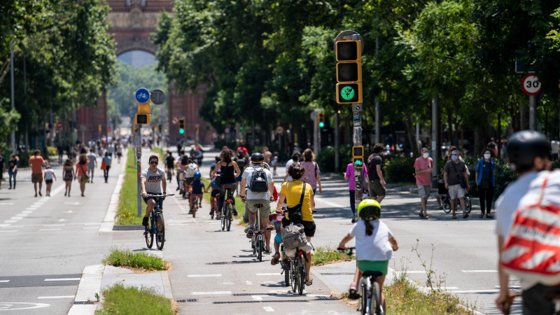 Carril bici central del passeig de Sant Joan, que forma part de la xarxa d'itineraris segurs per a vianants, amb ciclistes de totes les edats pedalant. Als laterals de la calçada, gent passejant 